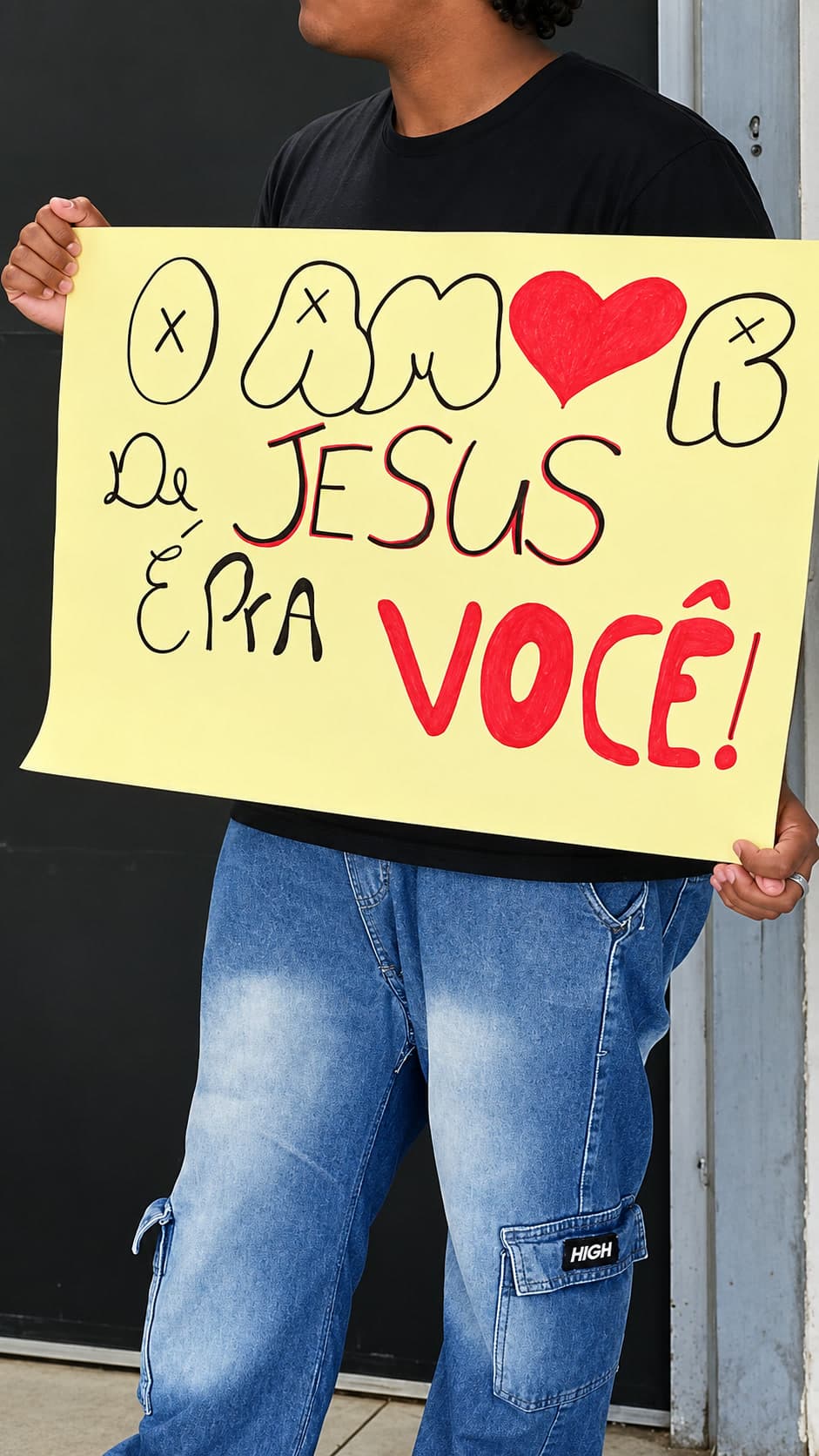 Jovem na rua segurando um cartaz escrito: O amor de Jesus é pra você!